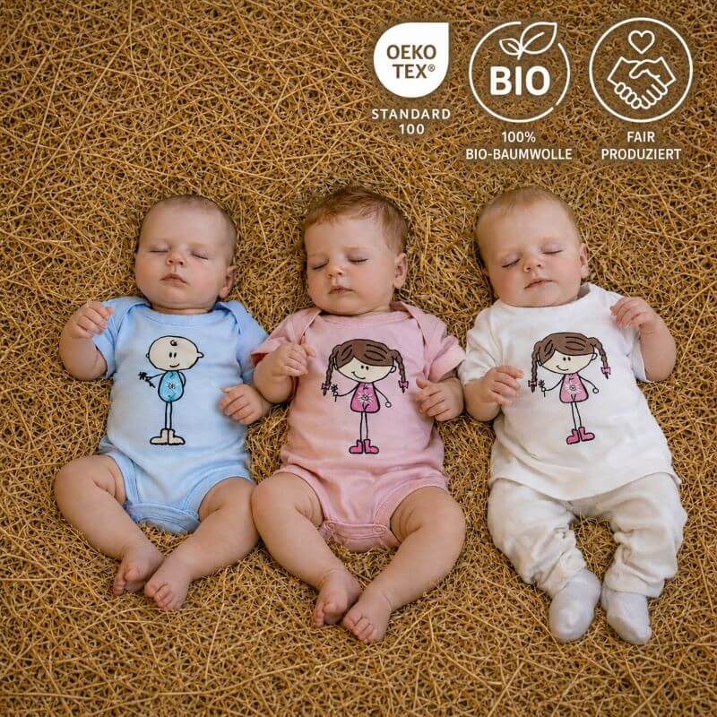 Drei Babys liegen nebeneinander auf einer natürlichen Unterlage aus Heu und tragen Baby Bodys aus Bio-Baumwolle in Blau, Rosa und Weiss mit liebevollen Figurenmotiven.